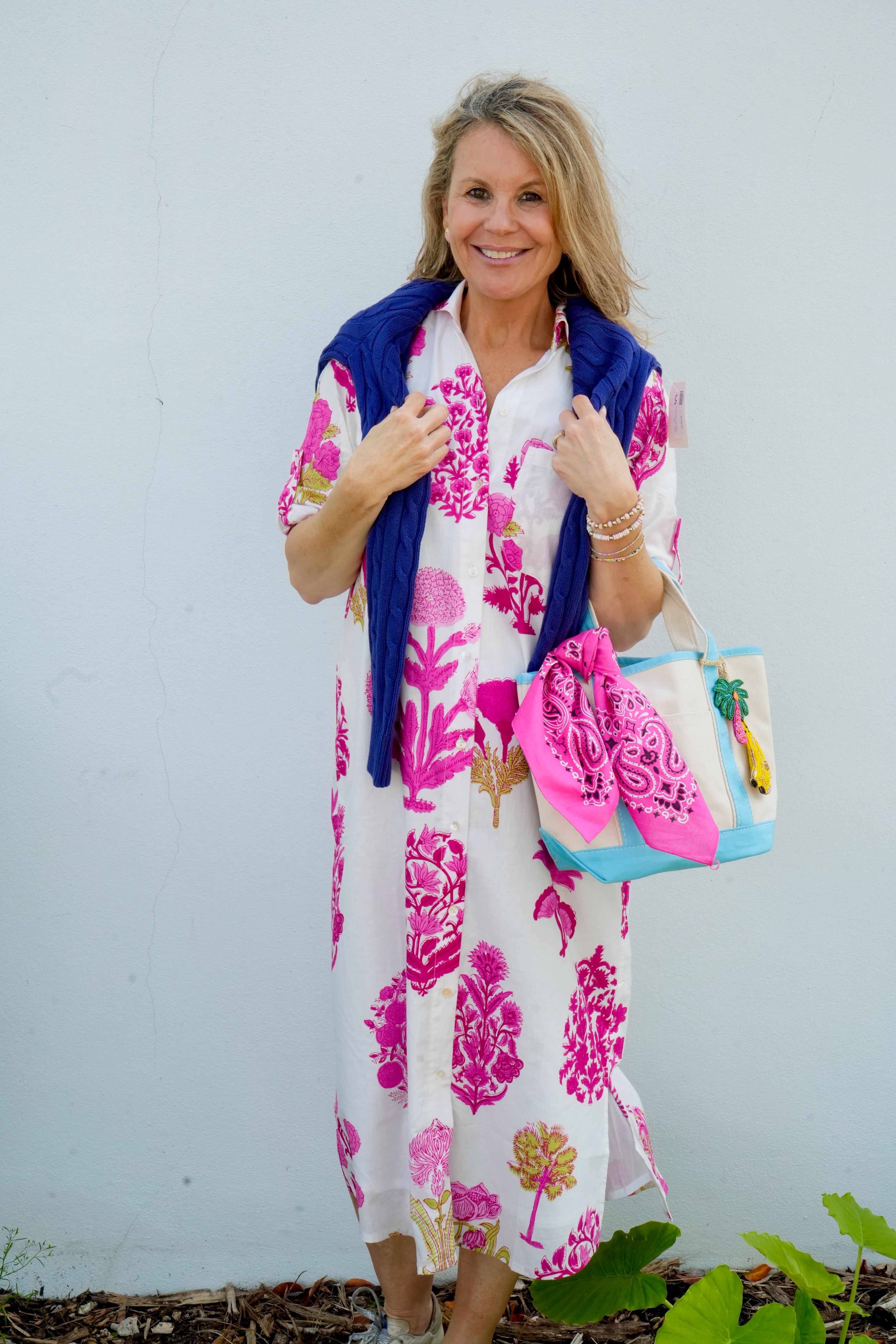 Woman wearing a floral dress with a blue cardigan and colorful bag against a white background