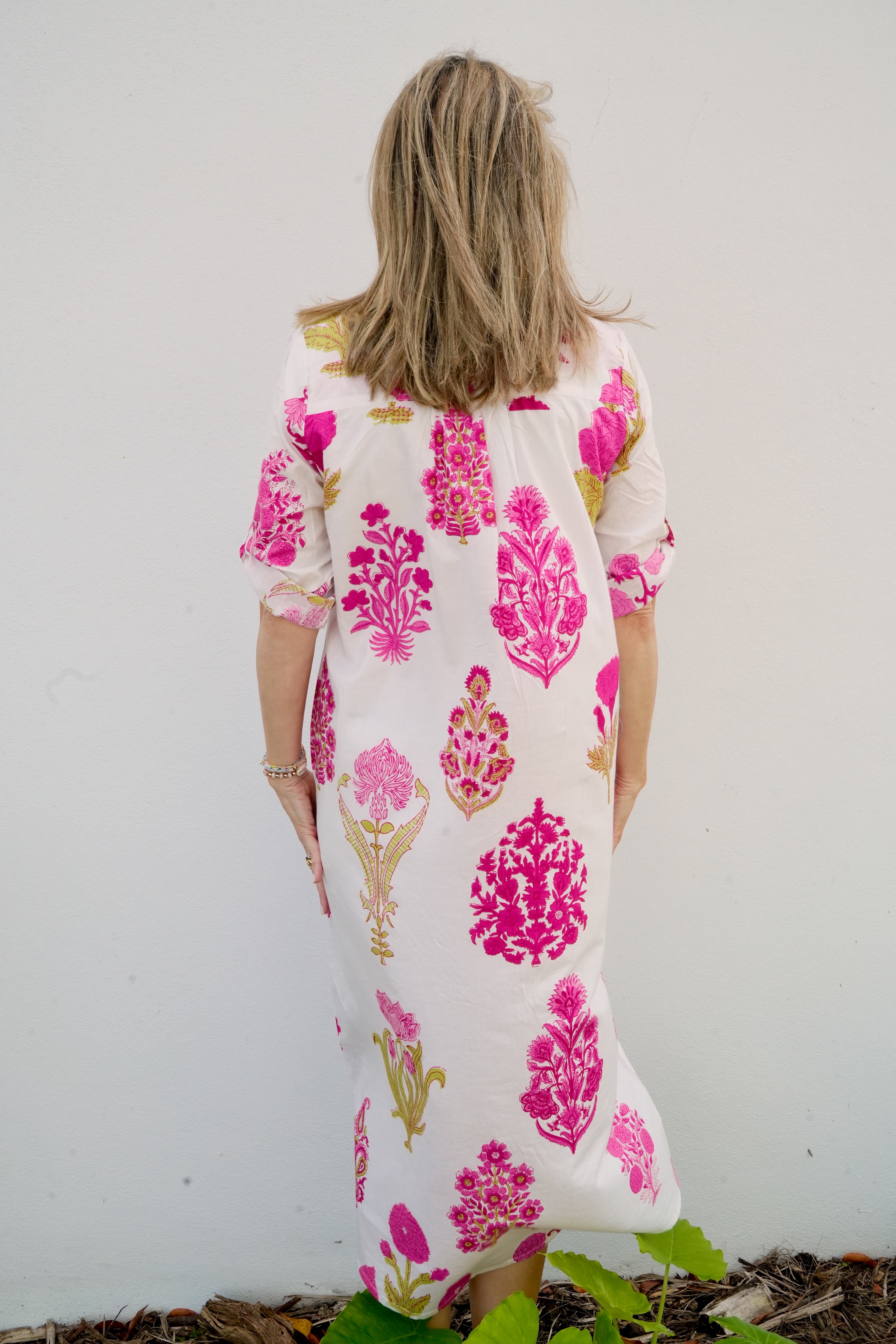 Woman wearing a white dress with pink floral patterns against a plain background