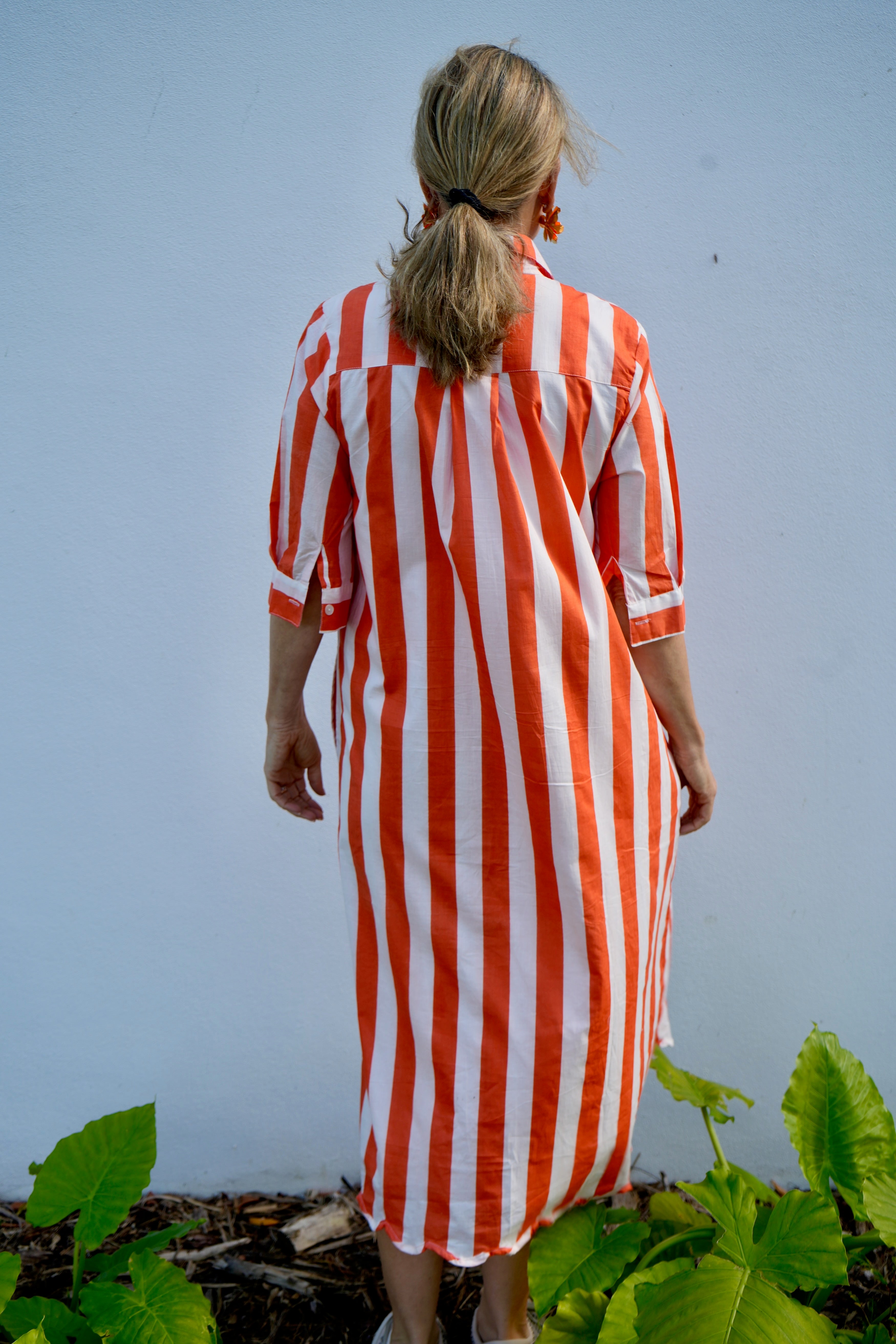 Person wearing a red and white striped dress standing outdoors with a light blue background