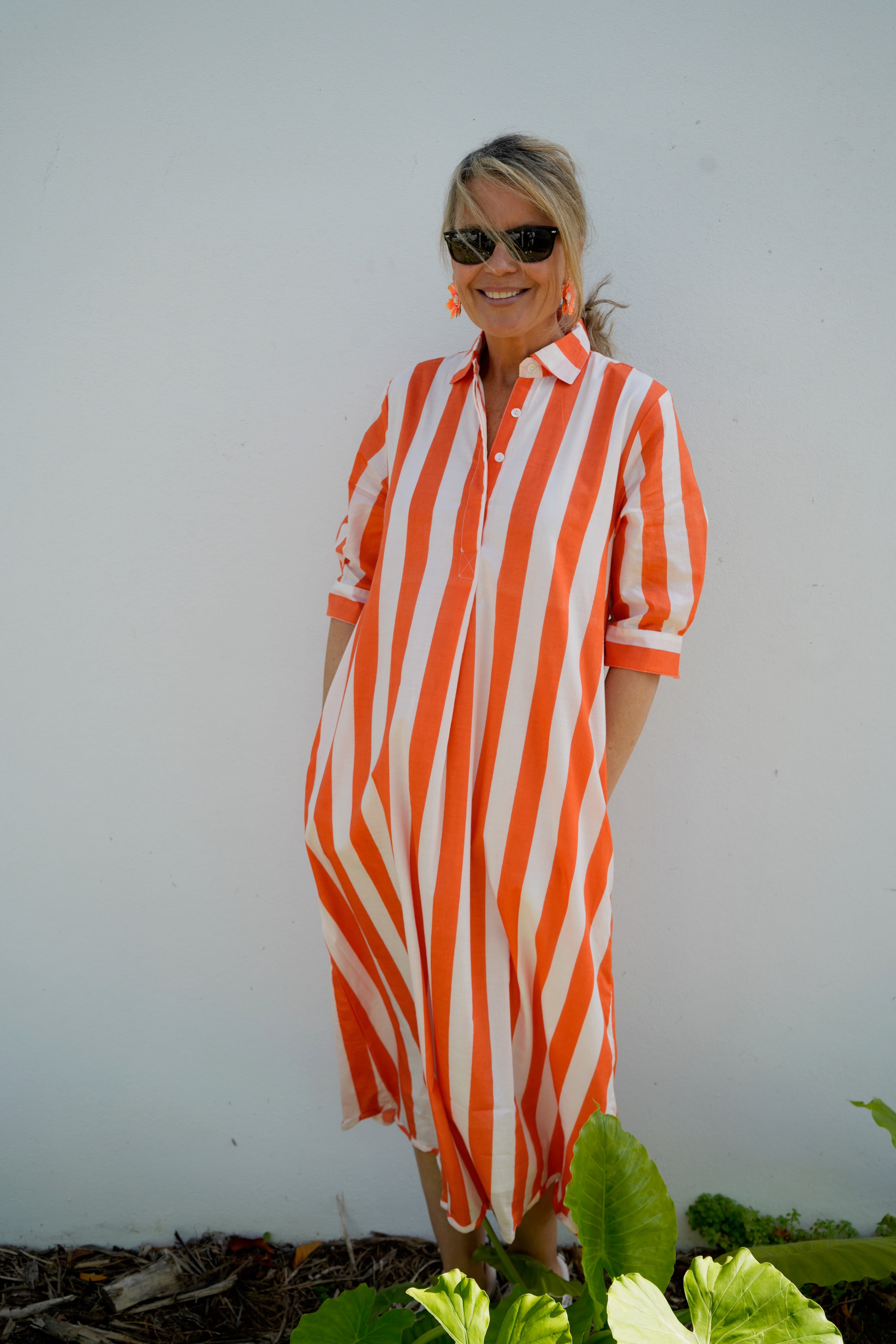 Woman wearing an orange and white striped dress standing in a garden.