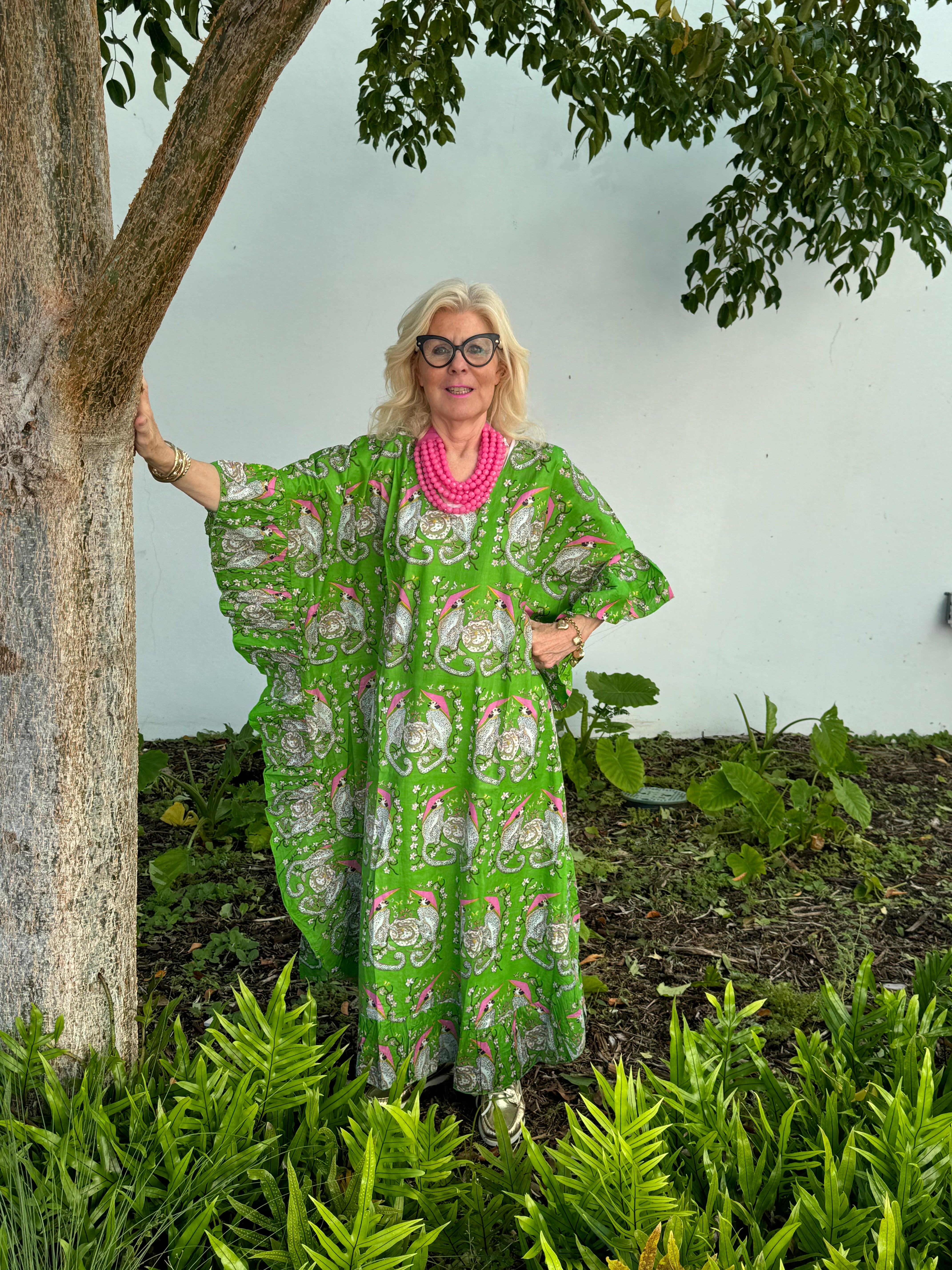 Woman in a green patterned dress standing next to a tree in a garden.