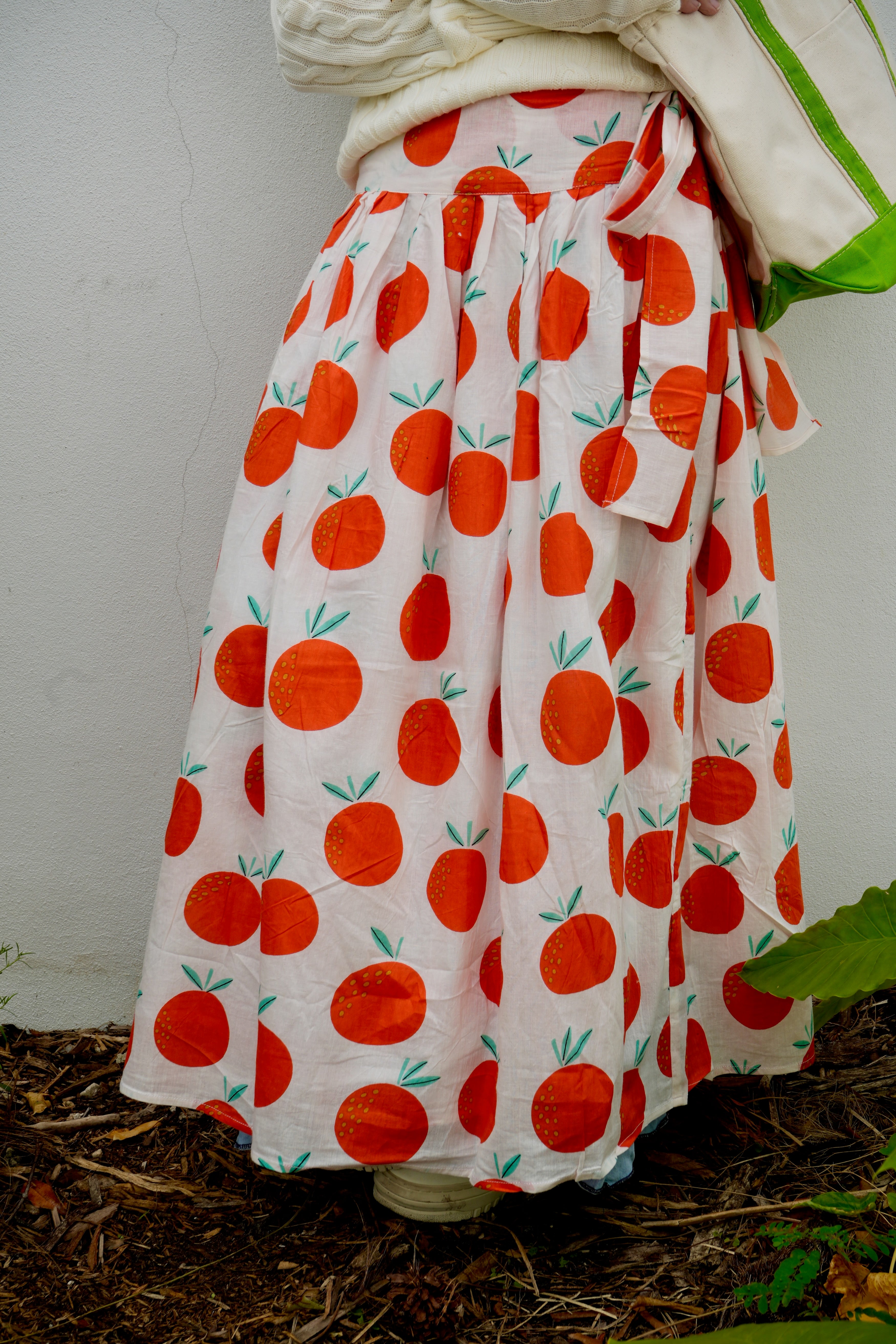 Person wearing a skirt with oranges pattern on a white background