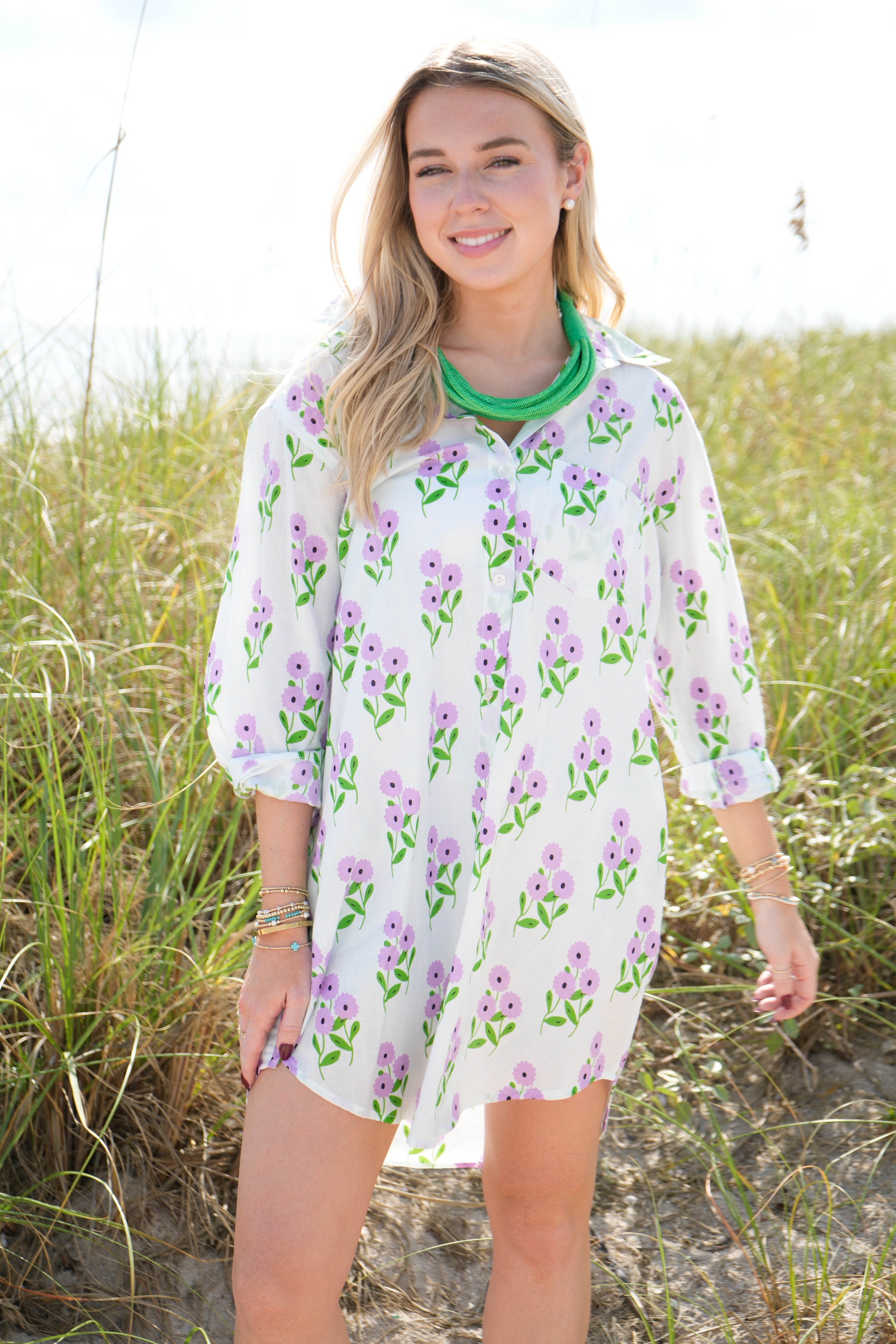 Woman wearing a floral dress standing on a beach with grass in the background