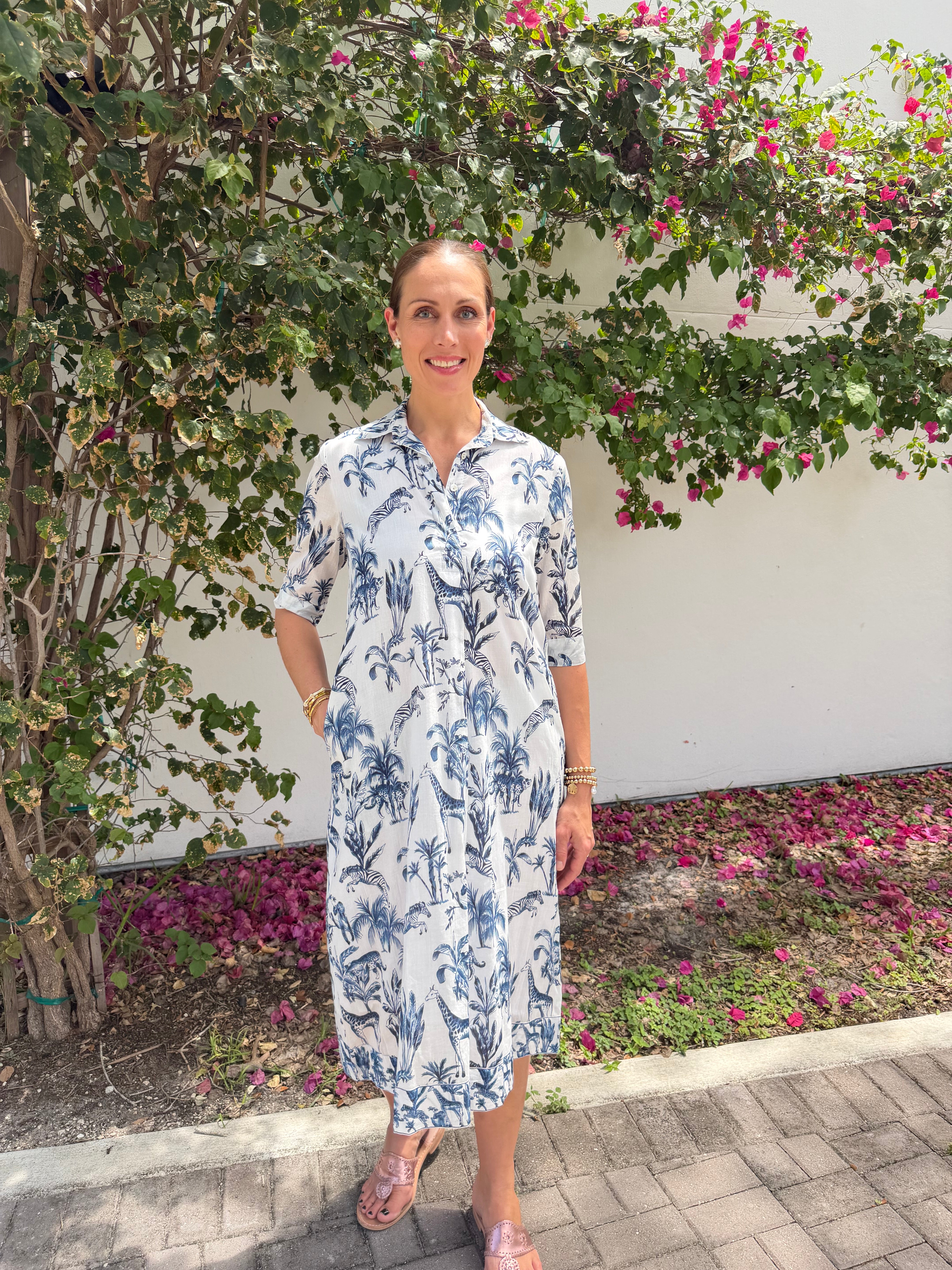 Woman in a floral dress standing in front of a garden with pink flowers.