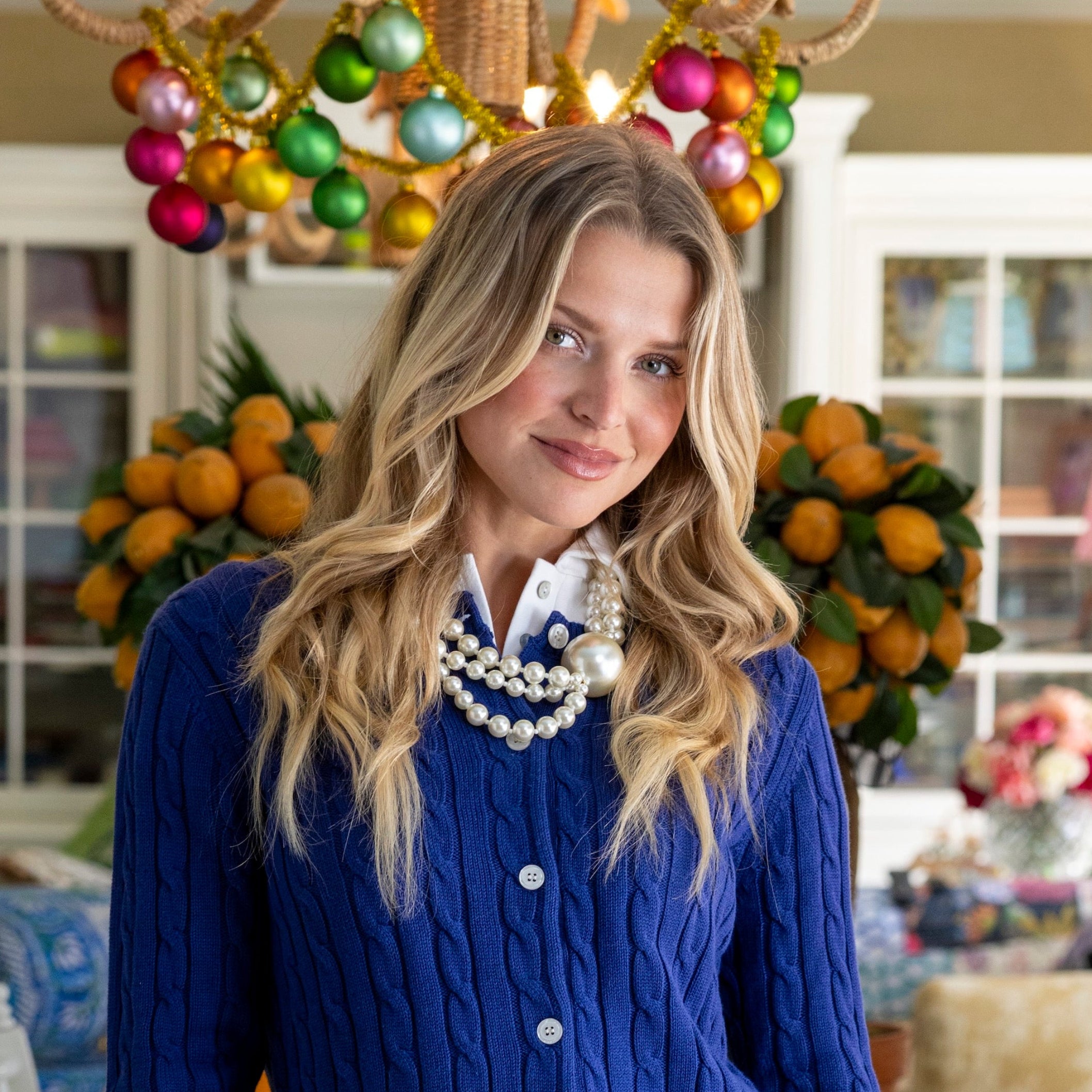 Woman in a blue cardigan and patterned skirt standing in a decorated room with a dining table and chairs.