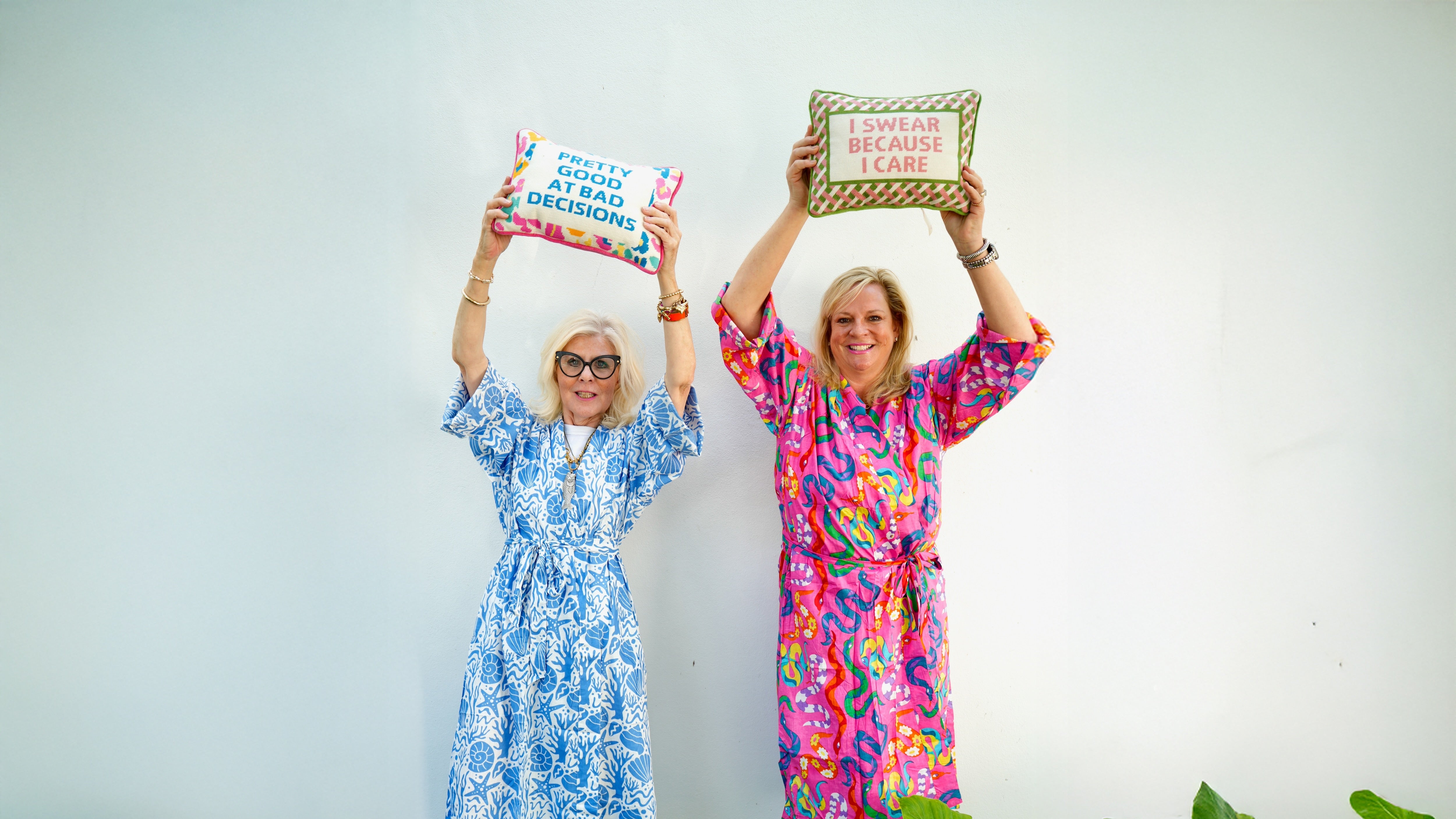 Two women in colorful dresses holding signs with text, standing in a garden.